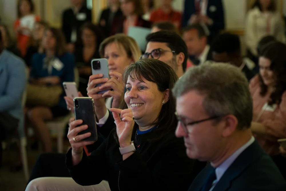 Guests watch a presentation, some holding phones.