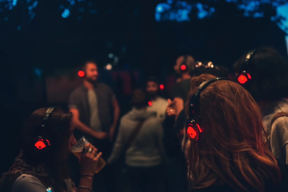 Participants wear illuminated headphones at an outdoor evening event.