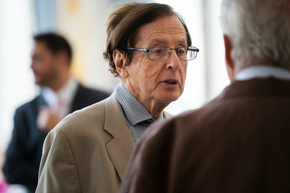 A guest in a beige jacket talks with another attendee.