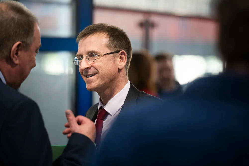 Two men in suits talk among the guests.