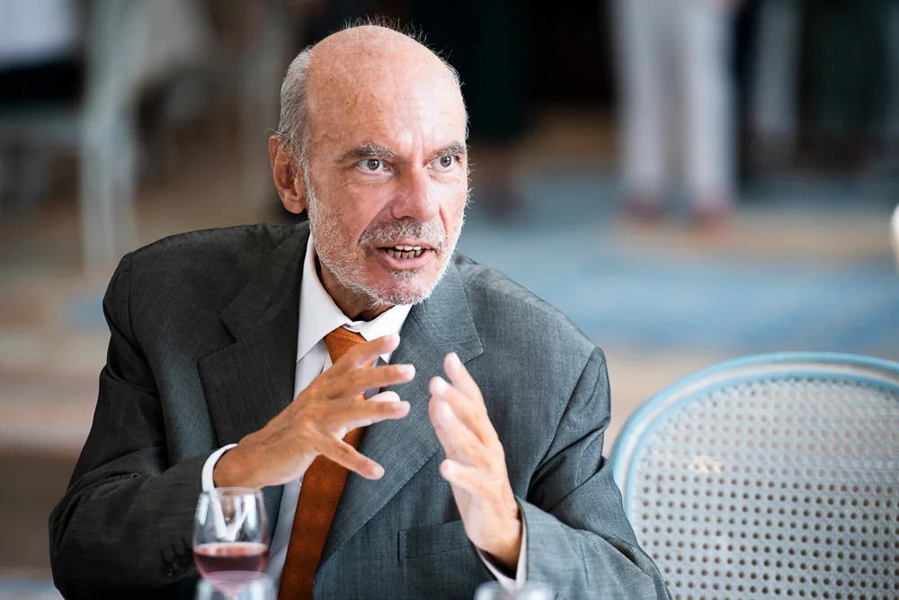 A man in a suit and orange tie during a conversation.