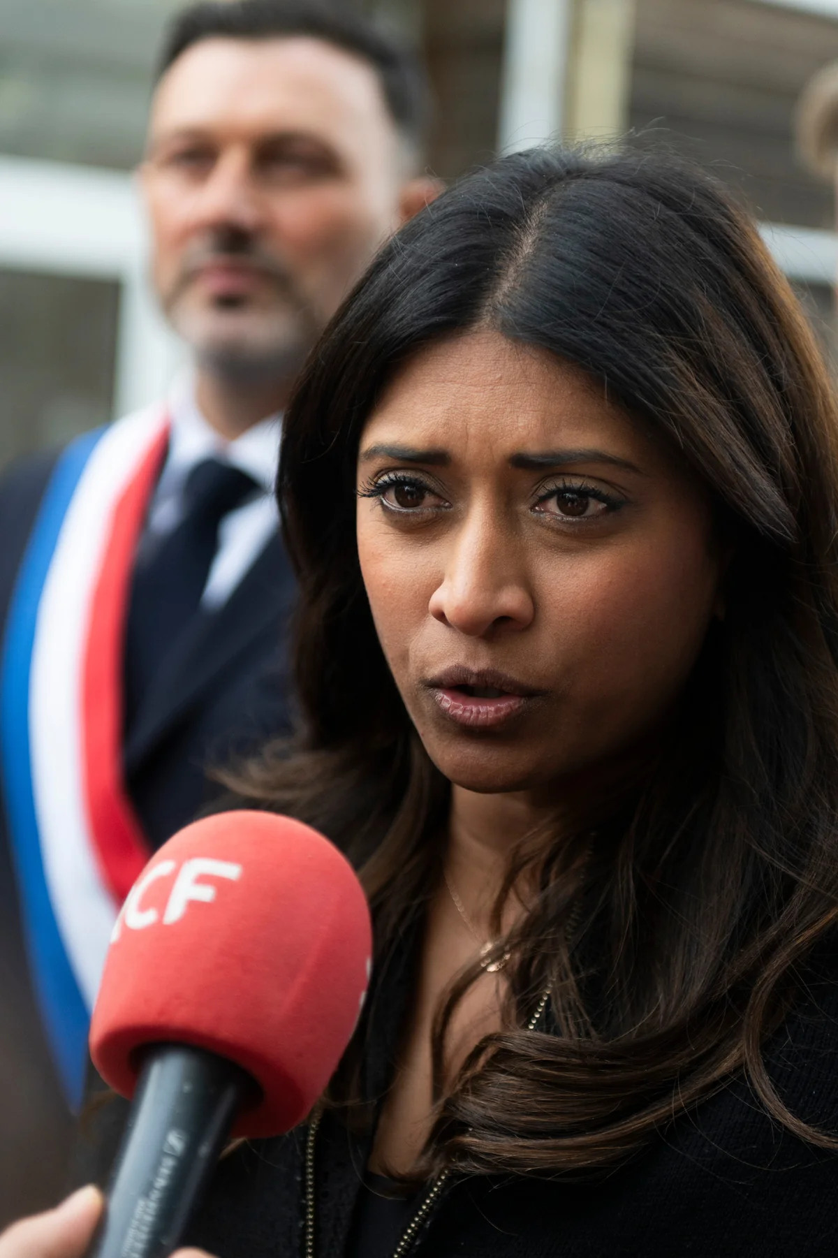 A woman answers questions in front of a microphone.