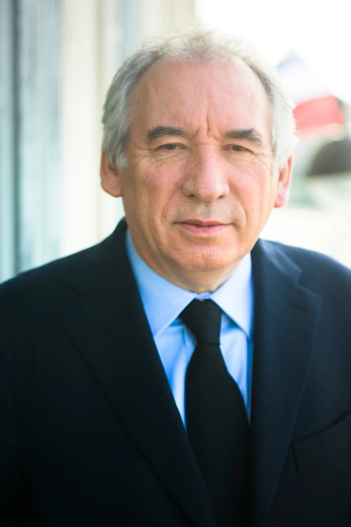 Portrait of a man in a suit and tie beside a window.