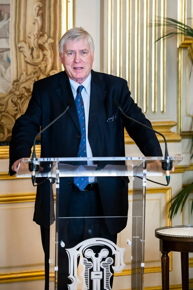 A speaker at a lectern in front of gilded panelling.