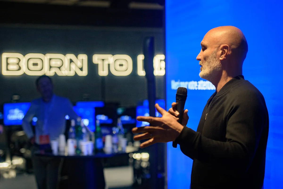 A speaker holding a microphone in front of a blue screen.
