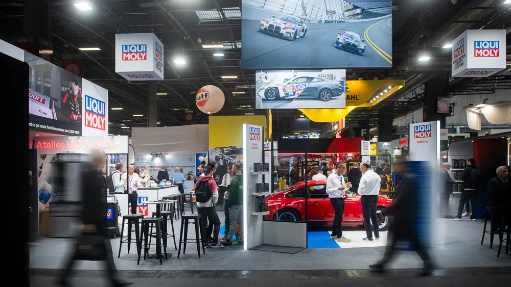 Visitors and exhibitors around a red car at the LIQUI MOLY stand.